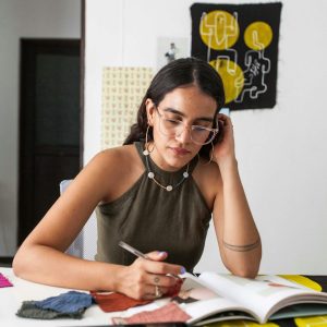 Young woman designer working thoughtfully with fabric swatches at studio.